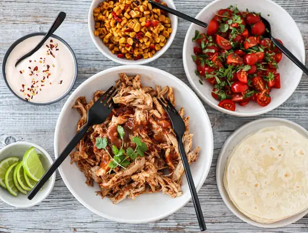 Pollo desmenuzado con ensalada de tomate y ensalada de maíz y pimentón