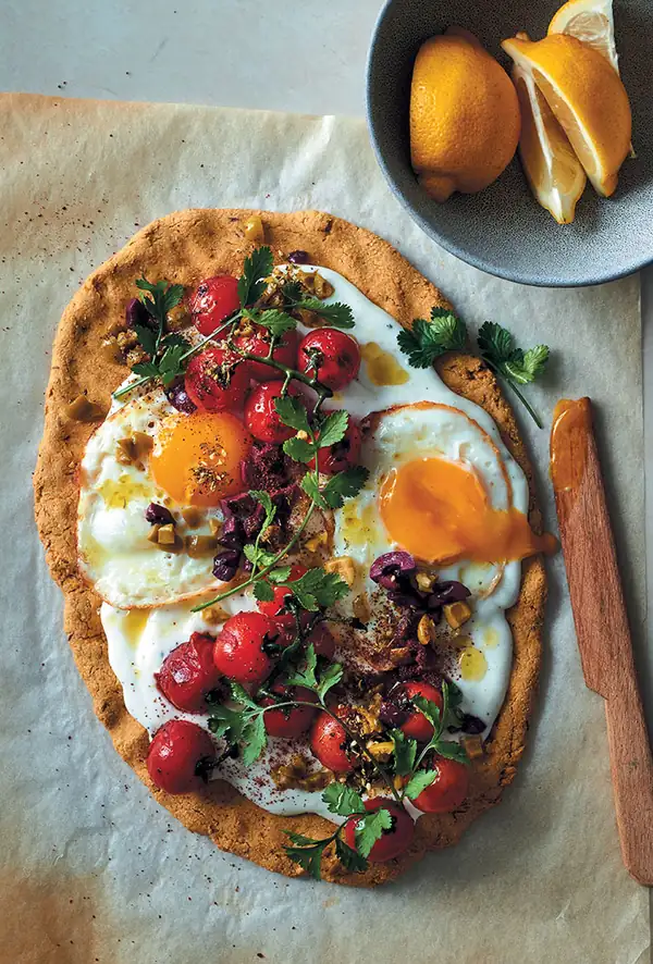 Chickpea flour flatbread topped with garlicky yoghurt, fried eggs, vine tomatoes and olives