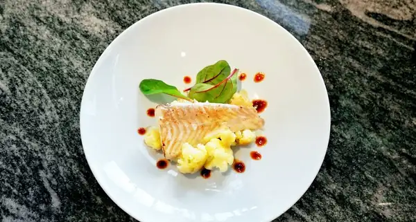 Disfrútalo con halibut entero asado al horno con especias, acompañado de coliflor cremosa y glaseado de mariscos