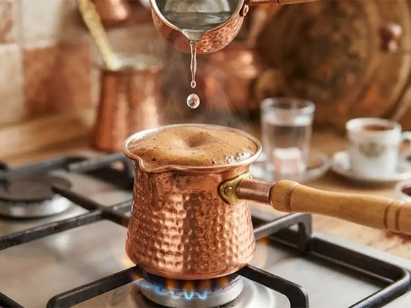 Why is a drop of cold water added to the coffee pot when brewing coffee?