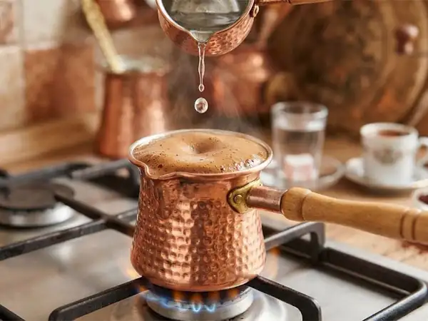 Why is a drop of cold water added to the coffee pot when brewing coffee?