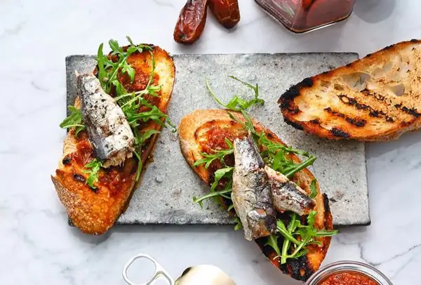 Sun-dried tomato and date pesto on baguette with arugula and oil-packed sardines